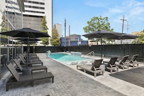 A rooftop pool area with lounge chairs and umbrellas, surrounded by a high fence, and buildings in the background. - VCAY - Bridge View 5BR-5BA  (New Orleans)