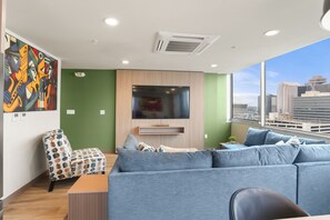 A modern living room with a large grey sofa, a small round table, and a flat-screen TV mounted on the wall. - VCAY - Bridge View 5BR-5BA  (New Orleans)