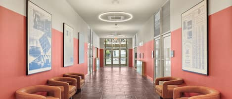 A hallway with a row of armchairs, framed pictures on the walls, and a ceiling light fixture.