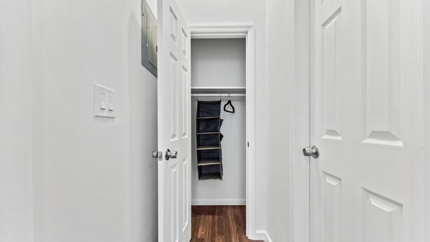 A hallway with white walls, a wooden floor, and a closet with hanging storage.