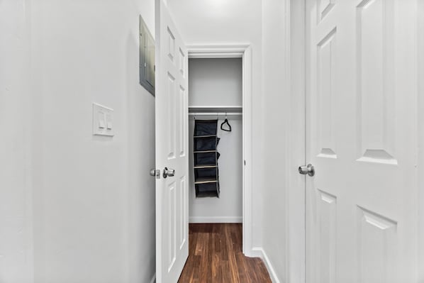 A hallway with white walls, a wooden floor, and a closet with hanging storage.