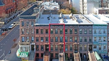 A multi-story building with a red facade, a green awning with 'F&L Mini Market Corp' signage, and a fire escape on the ground floor.