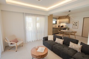 A modern living room with a sofa, a chair, a dining table, and a kitchen area.