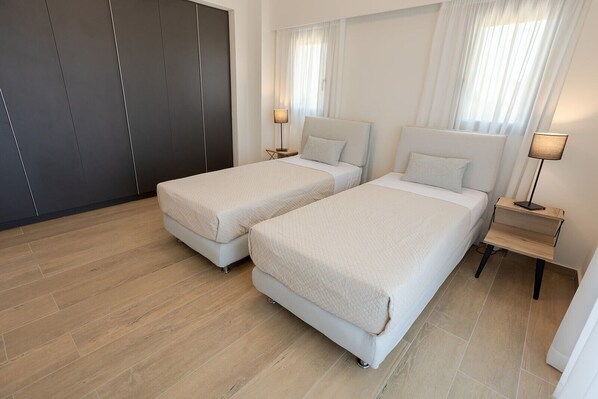 A hotel room with two beds, a wardrobe, and a nightstand with a lamp.