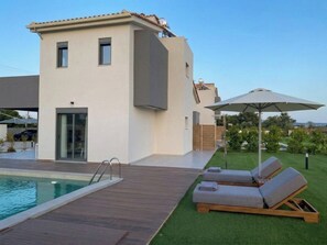 A modern house with a swimming pool, outdoor lounge chairs, and a well-maintained lawn.