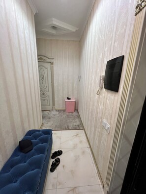 Ein schmaler Flur mit einer blauen gepolsterten Bank, einem pinken Mülleimer und einem an der Wand befestigten Fernseher.