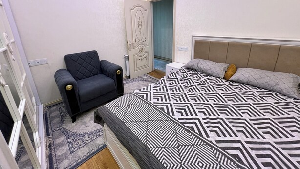 A bedroom with a bed, a chair, a door, and a window. - A&P APARTMENT (Bakı)