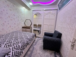 Ein Schlafzimmer mit einem Bett, einem Nachttisch, einer Kommode, einem Kleiderschrank und einem schwarzen Sessel.