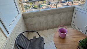 A balcony with a view of a cityscape, a table with a pink bucket, and a black chair. - A&P APARTMENT (Bakı)