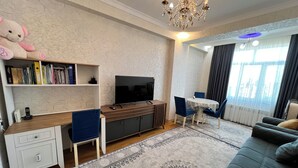 A modern living room with a flat-screen TV, a wooden desk, a sofa, and a dining area with a table and chairs. - A&P APARTMENT (Bakı)