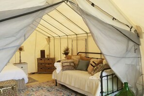 Une pièce aménagée avec une tente, un lit, une table de chevet, une commode et une lampe.