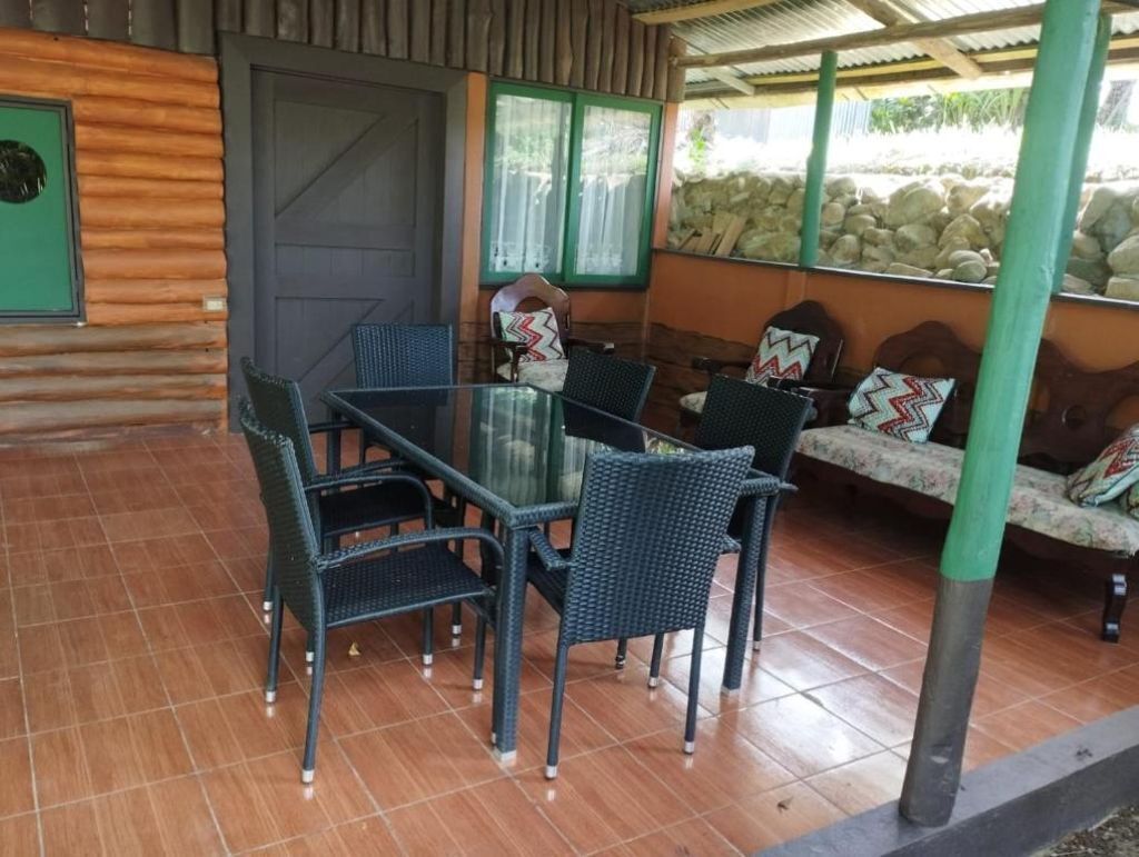 Un espace extérieur abrité, avec une table à plateau de verre et des chaises en osier, un mur en pierre et une porte verte.