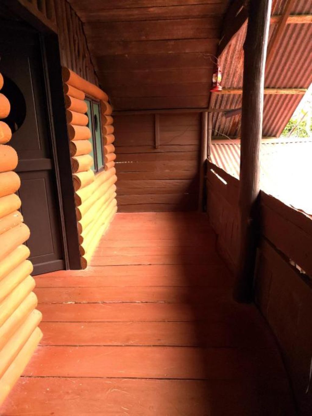 A wooden log cabin interior with a wooden floor and a door leading to a balcony.