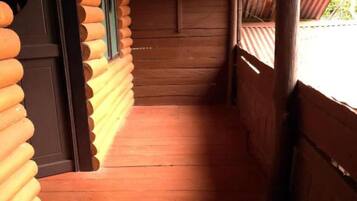 A wooden log cabin interior with a wooden floor and a door leading to a balcony.