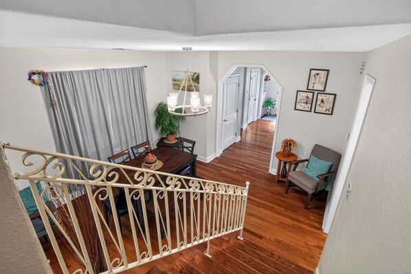 Uma ampla sala de jantar com uma mesa e cadeiras de madeira, um lustre e uma escada que leva a um andar superior.