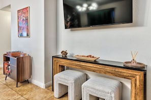 A modern living room with a flat-screen TV mounted on the wall, a wooden console table with a decorative bowl and reed diffuser, and a bookshelf with vinyl records. - Tropical Boho 3 bdrm house w/pool and pets are welcome. (Las Vegas)