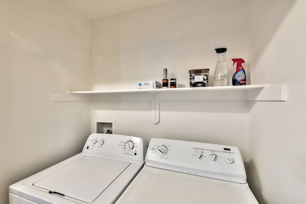 A laundry room with two white washing machines, a shelf with cleaning supplies, and a door leading to the laundry area. - Tropical Boho 3 bdrm house w/pool and pets are welcome. (Las Vegas)