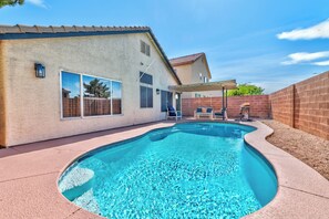 Ein Pool mit geschwungener Kante, eine Terrasse mit Stühlen und ein überdachter Sitzbereich.