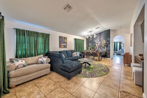 A spacious living room with a sectional sofa, a coffee table, and a dining area with chairs. - Tropical Boho 3 bdrm house w/pool and pets are welcome. (Las Vegas)