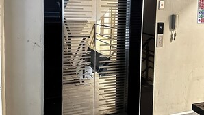 Ein Sicherheitshinweisschild über einer Tür mit einem Metallgitter, dahinter ein Treppenhaus und ein an der Wand montiertes Gegensprechanlage.