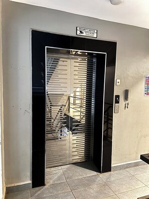 A security notice sign above a door with a metal gate, a stairwell visible through the gate, and a wall-mounted intercom. - Elegant Studio in kiambur road,fast Wifi & Free Parking (Nairobi)