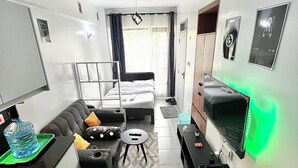 Ein kleines Hotelzimmer mit Bett, Sofa, Tisch, Fernseher und einer Küchenzeile.