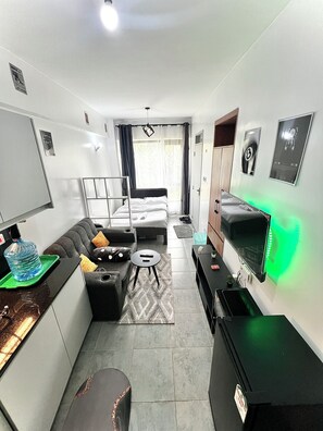 A compact hotel room with a bed, a sofa, a small table, a TV, and a kitchenette. - Elegant Studio in kiambur road,fast Wifi & Free Parking (Nairobi)