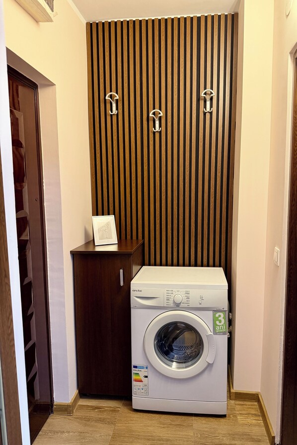 A laundry room with a front-loading washing machine, a wooden slat wall, and a small cabinet with a framed picture.