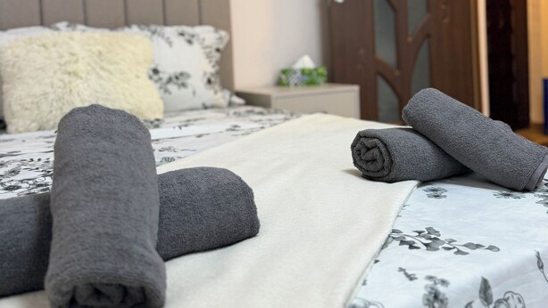 Una cama bien hecha con toallas enrolladas, una colcha estampada con motivos florales y una puerta de madera al fondo.