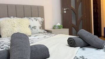 Un lit bien fait, avec des serviettes pliées en rouleaux, une couvre-lit à motifs floraux et, au fond, une porte en bois.