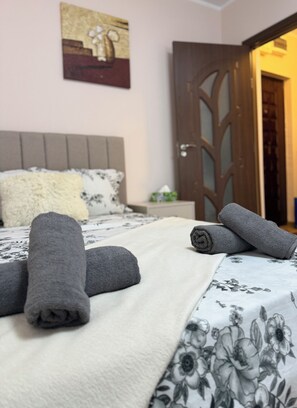 Una cama bien hecha con toallas enrolladas, una colcha estampada con motivos florales y una puerta de madera al fondo.