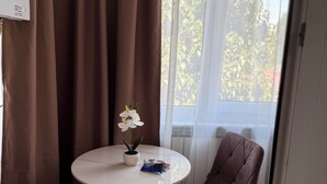 Una habitación con una mesa redonda, dos sillas, una orquídea en maceta y una ventana con cortinas.