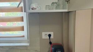 Una cocina con cafetera, tabla de cortar y ventana con persianas.