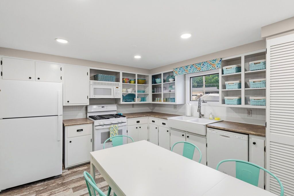 Una cucina moderna con mobili bianchi, un'isola centrale e sedie color petrolio.