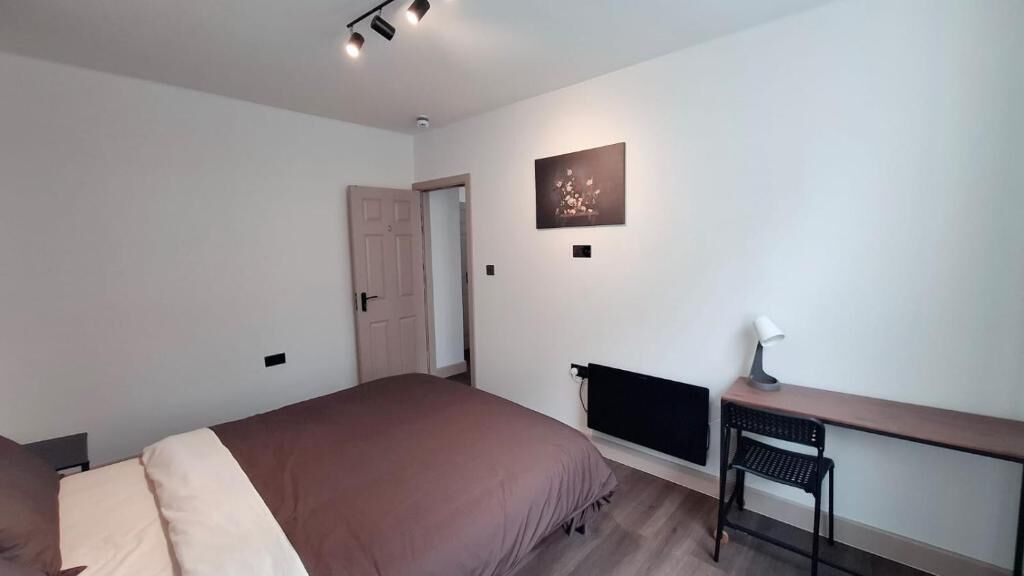 A bedroom with a bed, a desk, a chair, a radiator, and a door.