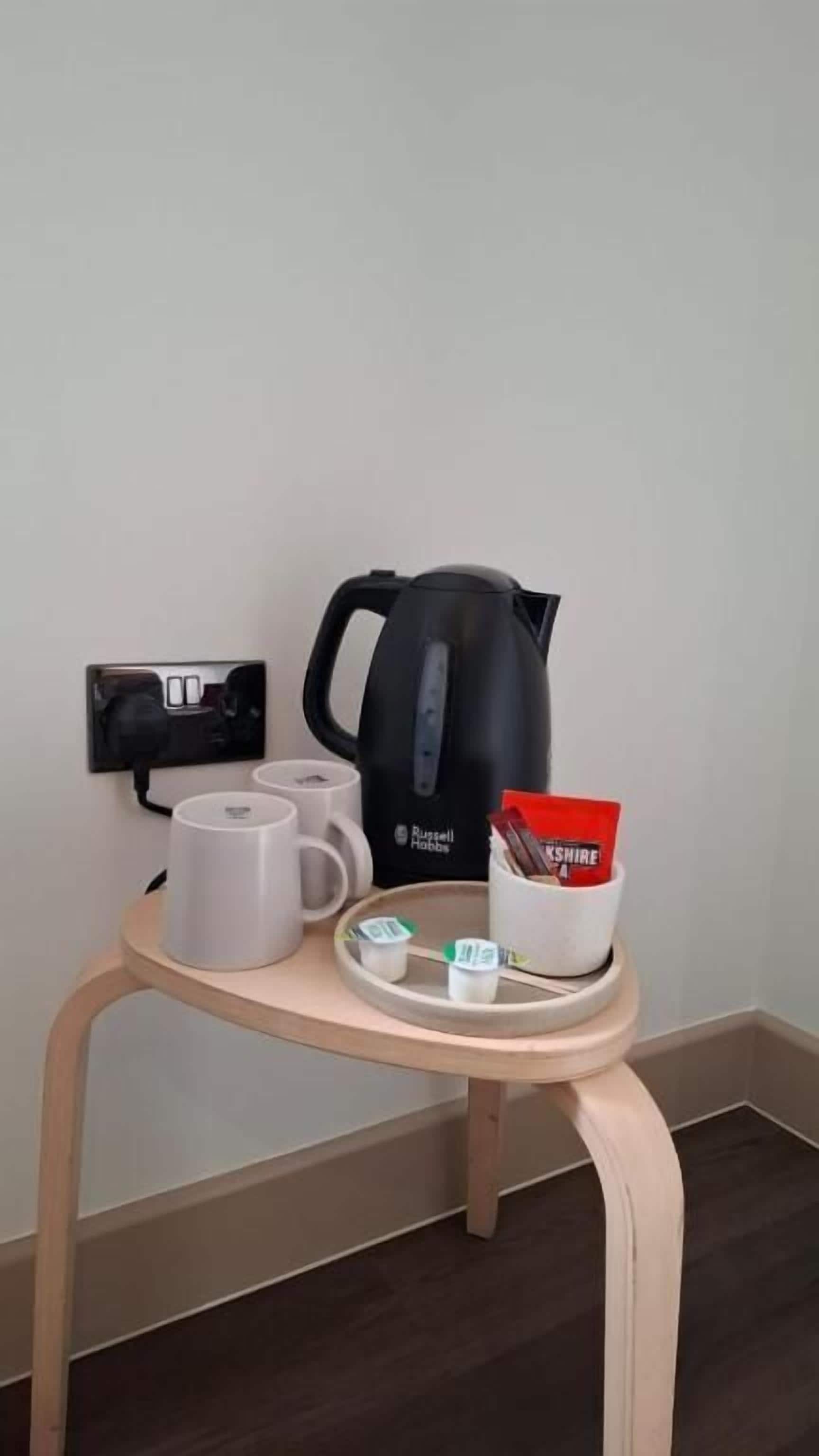 A small table with a kettle, two mugs, a tray with a packet of tea, and a power outlet.