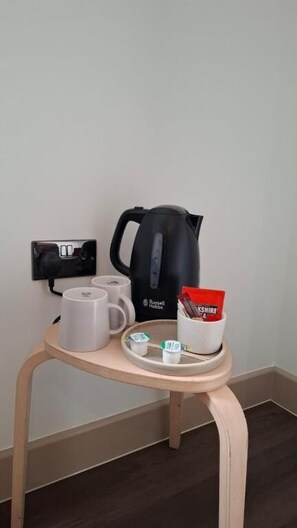 A small table with a kettle, two mugs, a tray with a packet of tea, and a power outlet.