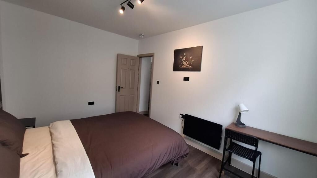 Un dormitorio con cama, escritorio, silla, radiador y puerta.