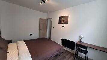 Un dormitorio con cama, escritorio, silla, radiador y puerta.