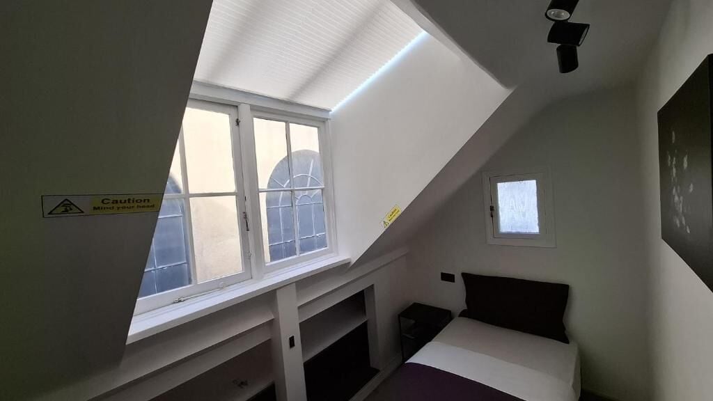 A room with a sloped ceiling, a bed, a window, and a caution sign on the wall.