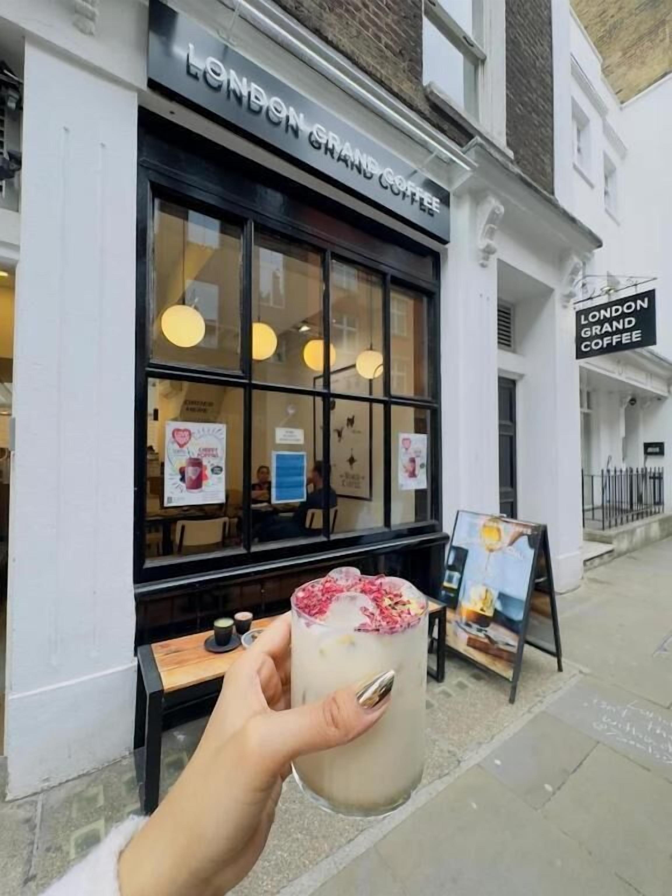 A storefront with a sign reading 'LONDON GRAND COFFEE' and a person holding a drink with a straw.