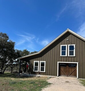 A two-story building with a gabled roof, a front garage door, and a covered porch area. - Tejas Hills Johnson City (Johnson City)