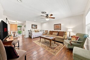 A living room with a ceiling fan, a sofa, a coffee table, and a television. - Tejas Hills #1 & #2 | Hill Country Pool Retreat (Fredericksburg)