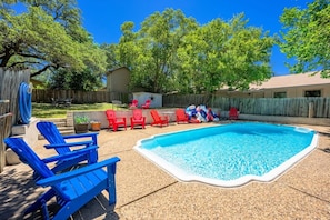 A backyard with a swimming pool, red and blue lounge chairs, and a wooden fence. - Tejas Hills #1 & #2 | Hill Country Pool Retreat (Fredericksburg)