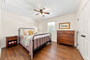 A bedroom with a bed, nightstand, dresser, and a ceiling fan. - Tejas Hills #1 & #2 | Hill Country Pool Retreat (Fredericksburg)