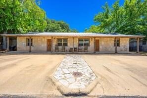 A two-story stone building with a covered porch, a stone pathway leading to the entrance, and a clear blue sky. - Tejas Hills #1 & #2 | Hill Country Pool Retreat (Fredericksburg)