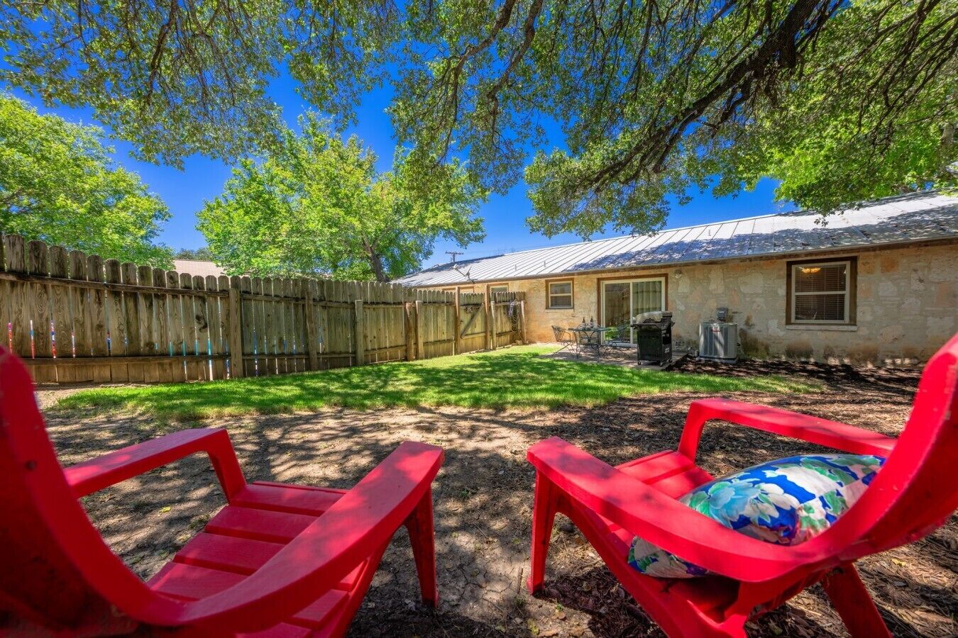 A backyard with a wooden fence, a house, and two red chairs.