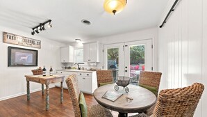 Una cocina con armarios blancos, una mesa de comedor con sillas de mimbre y una lámpara colgante.