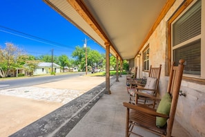 A covered porch with wooden chairs and a stone building. - Tejas Hills Guest Haus #2 | Hill Country + Pool (Fredericksburg)