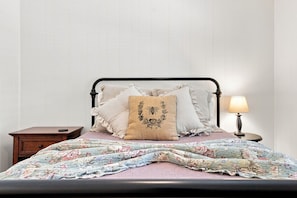 A bed with a floral quilt, a black metal frame, and several pillows, including one with a bee design. - Tejas Hills Guest Haus #2 | Hill Country + Pool (Fredericksburg)